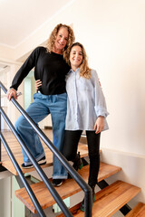 Two female coworkers smiling while posing standing on the stairs at office.