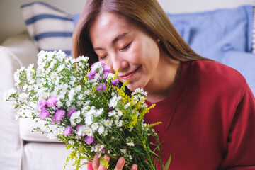 Portrait image of a beautiful young asian woman with closed eyes, holding and smelling flower bouquet