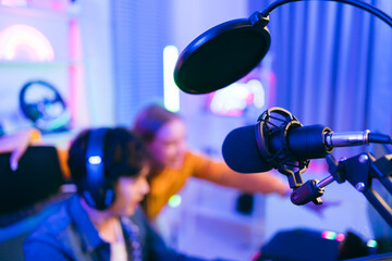 Close-up professional microphone with filter with blur teenager man and woman professional gamer prepare for competition in the background, for casting gameplay or recording a podcast.