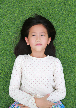 Portrait of Asian girl kid resting on green grass. Above view.