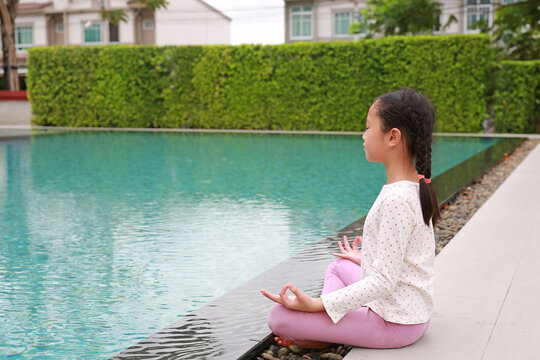 Peaceful Asian young girl kid practicing mindfulness meditation sitting near the pool.
