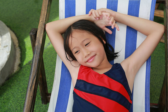 Portrait of Asian girl kid in swimsuit with wet hair lying on canvas bed near the pool.