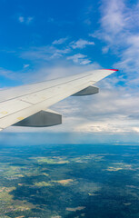 View of airplane wing, blue skies and green land during landing. Airplane window view.