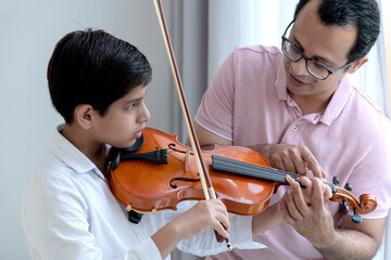 Indian teacher or father helping student playing violin indoor, musical education concept