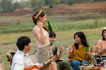 Happy group of young Asian friends party on vacation enjoy cheering with beer bottle. drinking at camping lake side. hands holding alcoholic beverages. Picnic in holiday.