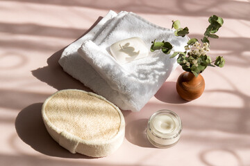 set of bath accessories in the sun with shadows, towel, washcloth, cream, soap, a bouquet of green branches in a vase