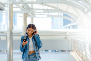 Young asian woman using headphone for listening nice music and walking in city. Girl happiness, smile face. Female love listen music that make her relax and enjoying life