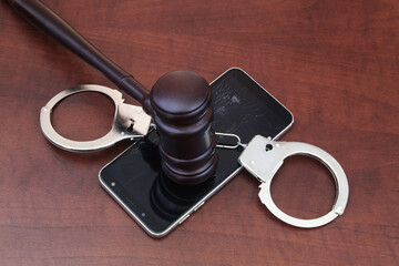 Broken smartphone with judge gavel and handcuffs. Laws and justice concept.