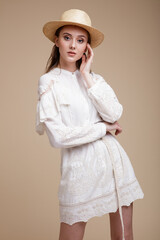 High fashion photo of beautiful elegant young woman in a pretty white dress with the sleeves, hat posing over beige brown background. Studio Shot, portrait.