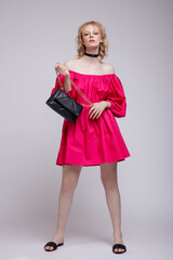 High fashion photo of beautiful elegant young woman in a pretty fuchsia pink dress, black handbag, clutch, choker posing over white, soft gray background. Studio Shot, portrait. Blonde