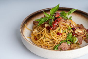 Spicy Thai basil pork pasta on white dish with white background. Italian food fusion Thai food. Tasty appetizing Italian fusion spicy spaghetti pasta with meat, chili, Thai basil. Italian fusion food.