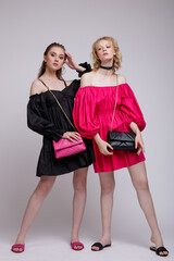 Two fashion models in pink fuchsia and black dress, choker, handbag, clutch. Beautiful young women. Studio shot, portrait. White, soft gray background.