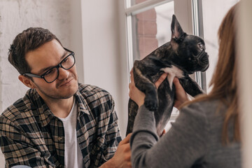Happy young couple having fun and playing with their French Bulldog puppy at home.Family,care,training,raising of animals concept.