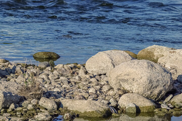 Close up of stacks of rocks on the river bank near dark blue wavy water stream on sunny day