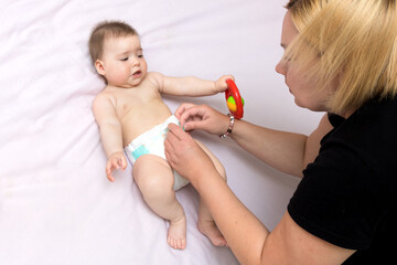 mom puts a diaper on the baby girl on the bed