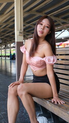 Young woman with long hair sits on a bench at a train station