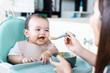 Baby enjoy and eating porridge in high chair.