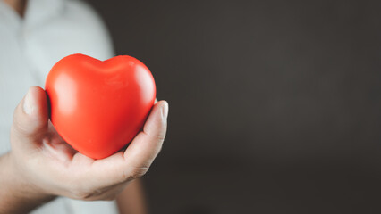 Man holding a red heart shape while standing with black background in the studio. Space for text. Donate, love, and encouragement concept