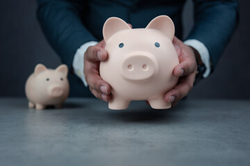 Businessman holding large piggy bank with small piggy bank placed on the table. Business finance and investment concept. Finance Savings concept. A businessman in suit is holding piggy bank.