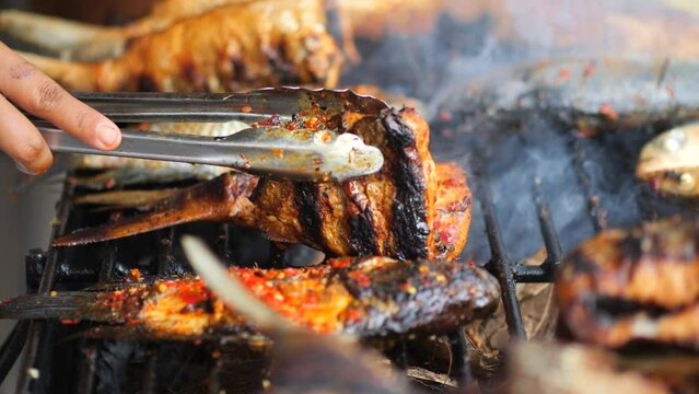 Close-up shot of cooking fish. Baking and roasting marinated fish on barbecue grill. Sea bass or grouper grilled over charcoal. 4K