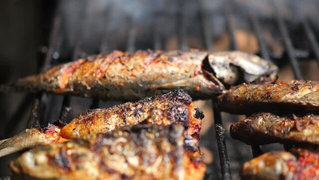 Close-up shot of cooking fish. Baking and roasting marinated fish on barbecue grill. Sea bass or grouper grilled over charcoal. 4K