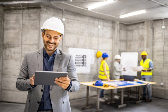 Successful architect or project manager in business suit and hardhat working on his tablet computer at construction site.