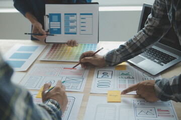 Close up ux developer and ui designer brainstorming about mobile app interface wireframe design on table with customer breif and color code at modern office.Creative digital development agency