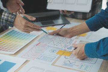 Close up ux developer and ui designer brainstorming about mobile app interface wireframe design on table with customer breif and color code at modern office.Creative digital development agency