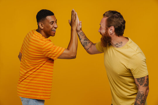 Two multinational male friends smiling and giving high five together