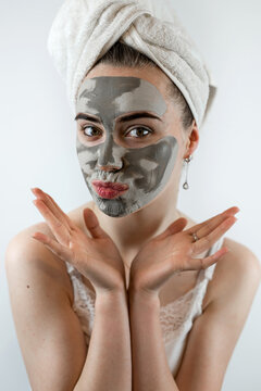 Young womanin white towel applying mud black mask on her face isolated on white, spa treatment