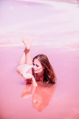 Obraz na płótnie Canvas Woman in a pink salt lake. She lies in a white bathing suit. Wanderlust photo for memory