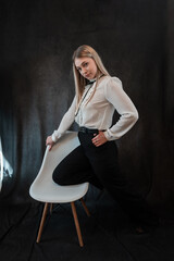 Portrait of seductive blonde caucasian woman sitting on chair isolated on dark background