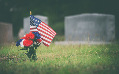 American flag and red, white and blue flowers on the veteran's grave. Honoring a fallen soldier in the cemetery on Memorial Day.