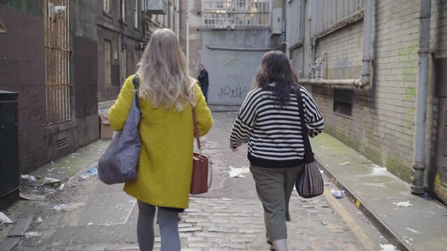 Two females walk along a alleyway followed closely by a suspicious man