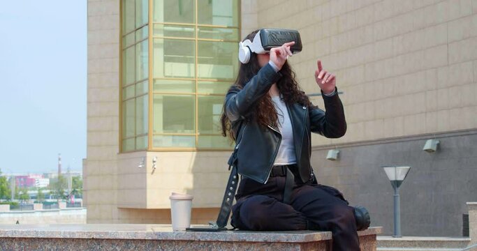 Young woman working in vr glasses in the midst of a bustling city. 4k footage of a modern technologies coming in our stillife. Escape from reality and digitalization of world.