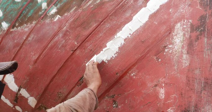 Close-up of a man repairing the hull of a wooden fishing boat