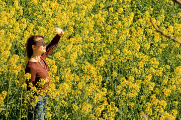 a young woman,of Caucasian race, walks through a rapeseed flowering field,as the sun is shining brightly,she looks into the distance through her palm,protecting herself from the bright rays of the sun