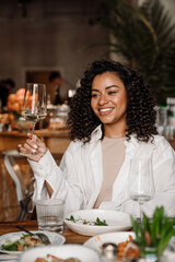 Young joyful african woman drinking wine while dining in restaurant