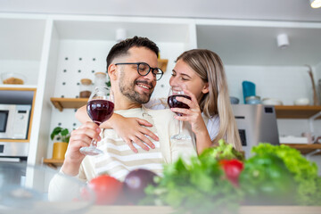 Smiling young couple cooking food in the kitchen together in the kitchen,having a great time together. Man and woman laughing and drinking Wine