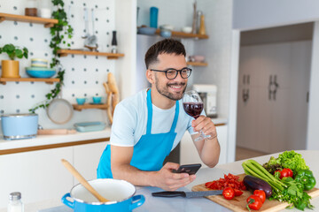 Head shot smiling young man using smartphone, chatting in social network while preparing food for vegetarian dinner at home. Happy millennial guy in eyeglasses web surfing recipe for meal in kitchen.
