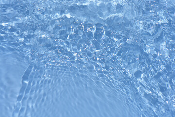 Blue water with ripples on the surface. Defocus blurred transparent blue colored clear calm water surface texture with splashes and bubbles. Water waves with shining pattern texture background.