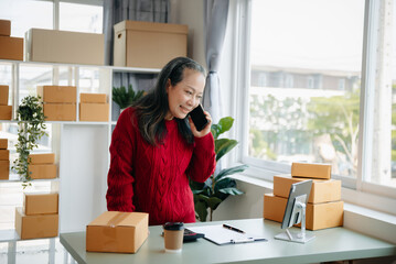 Mature business owner woman prepare parcel box and standing check online orders for deliver to customer on tablet, laptop Shopping Online