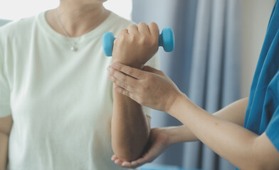 Obraz premium Old woman training with physiotherapist using dumbbells at home. Therapist assisting senior woman with exercises in nursing home. Elderly patient using dumbbells with outstretched arms.