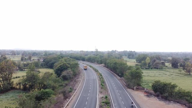Drone aerial view of a generic looking well maintained national highway of India with rural landscape of farmlands and lush green trees