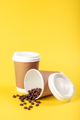Obraz na płótnie Canvas Disposable cups and scattered coffee beans on a yellow background isolated.