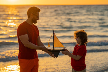 Father and son playing with toy ship on sea. Sunset silhouette of father son dreaming on cruise....