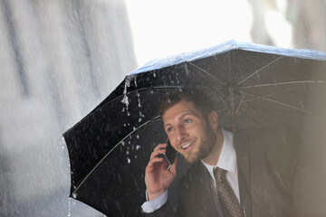 Businessman talking on cell phone under umbrella in rain