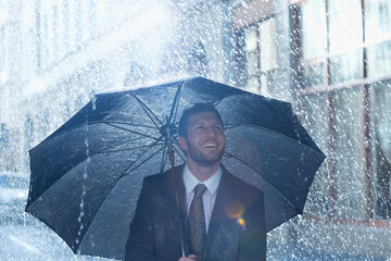 Happy businessman under umbrella in rain