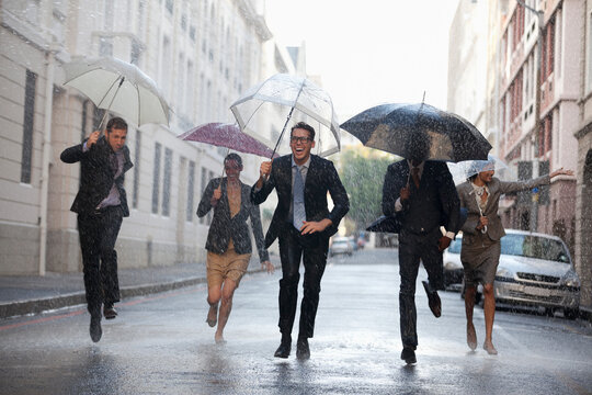 Business people with umbrellas running in rainy street