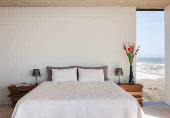 Vase of flowers next to bed in bedroom with ocean view - obrazy, fototapety, plakaty
